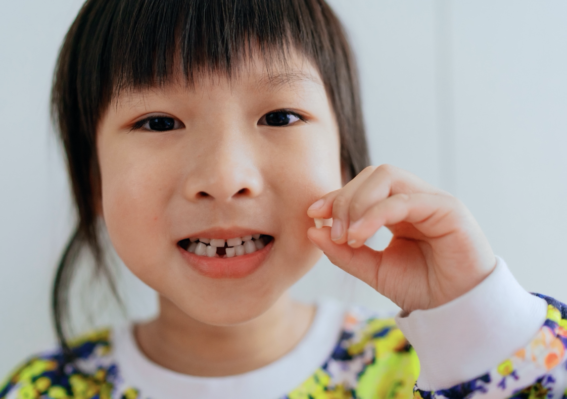 A young girl holding up a tooth she lost